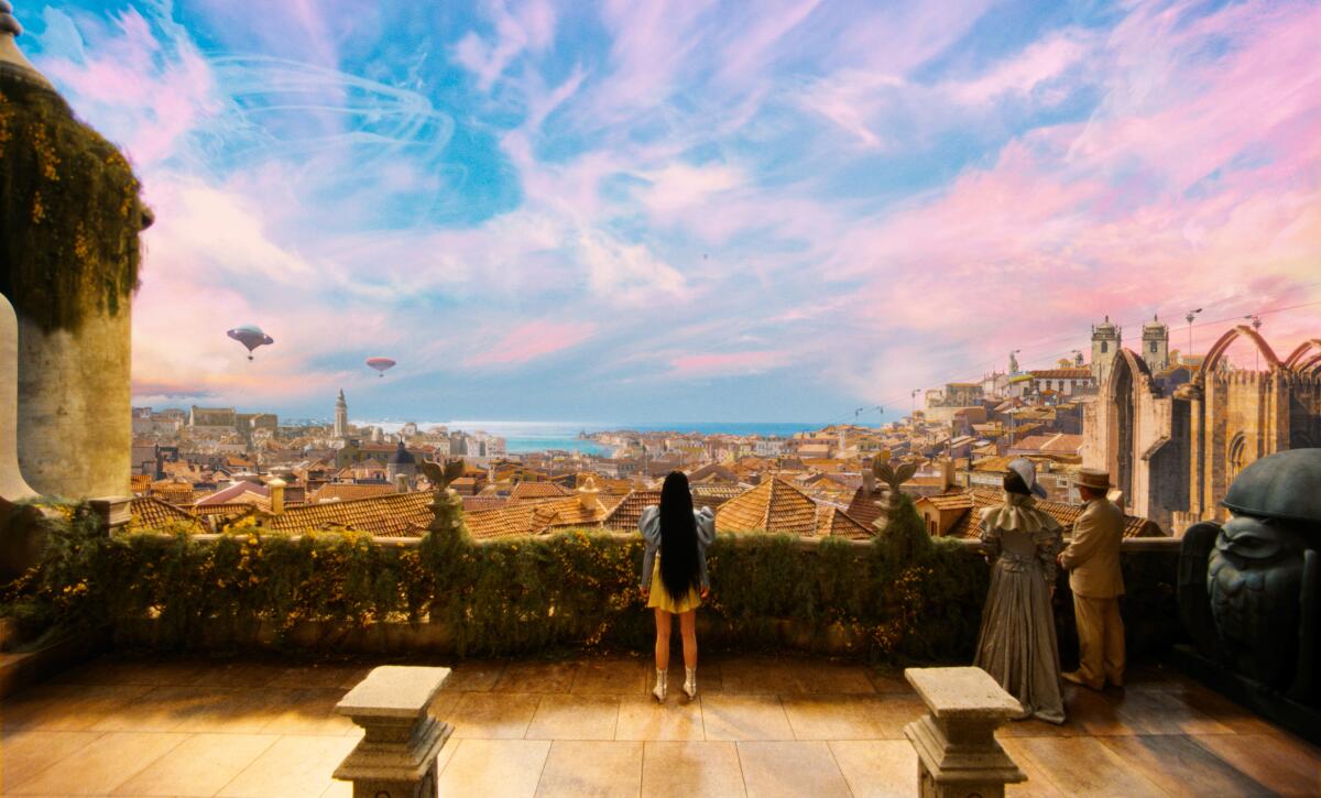 A woman looks out over a city scape beneath pink and blue skies in "Poor Things."
