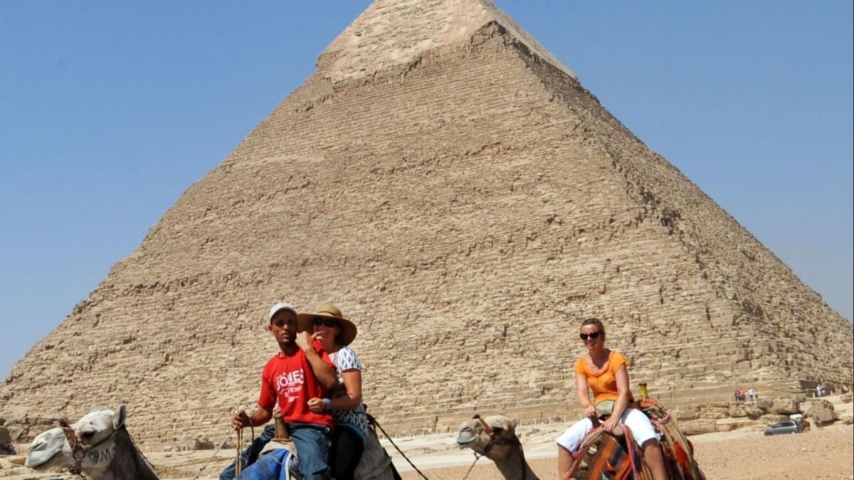Tourists and their guide ride camels past a pyramid in Giza, Egypt.