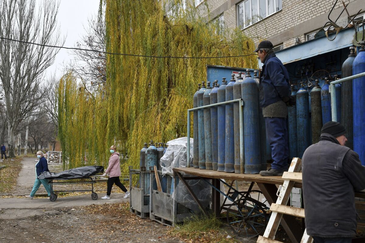 Workers stand by oxygen tanks for an ICU as medical staff carry a body of a patient who died of coronavirus on a stretcher, at the morgue of a hospital in Kramatorsk, Ukraine, Saturday, Nov. 6, 2021. Ukraine's health ministry has reported a one-day record of 793 deaths from COVID-19. Ukraine has been inundated by coronavirus infections in recent weeks, putting the country's underfunded medical system under severe strain. (AP Photo/Andriy Andriyenko)