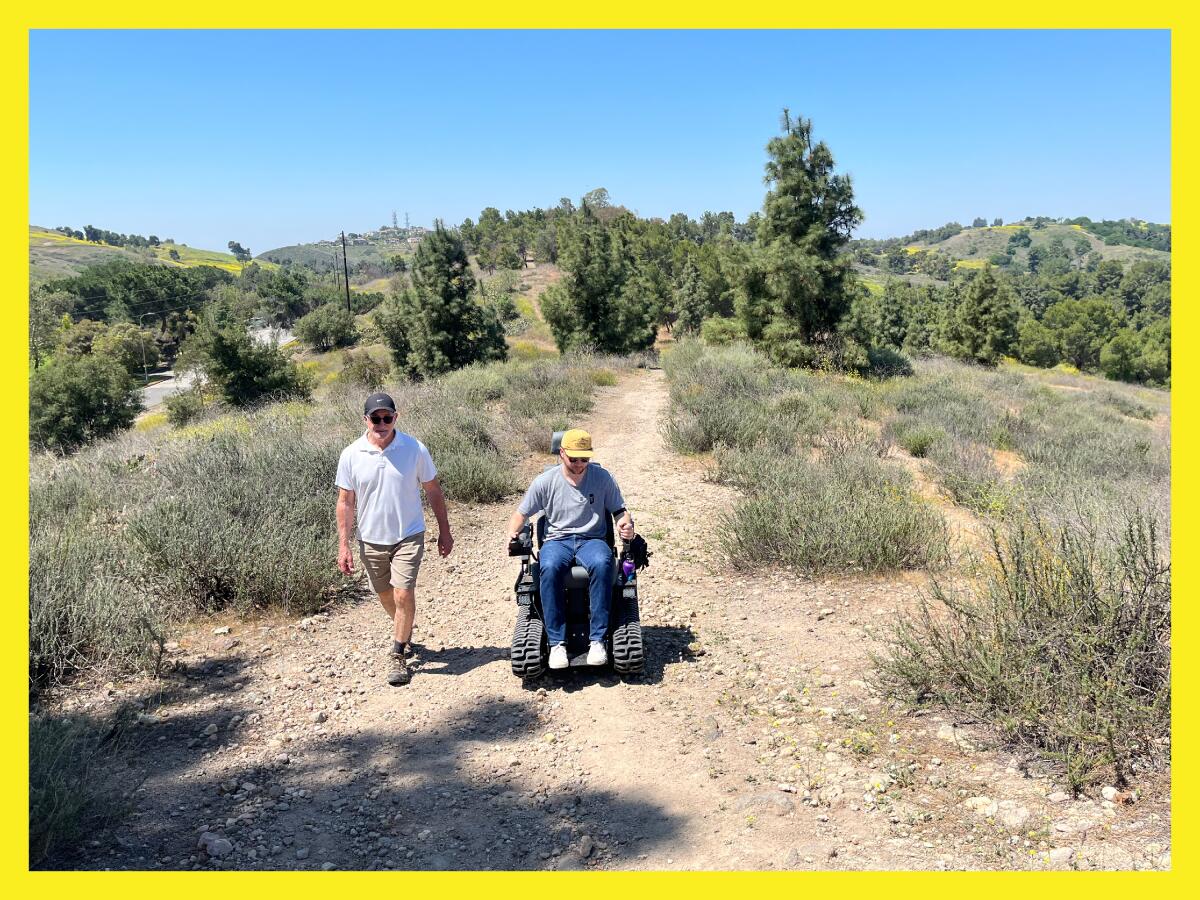 photo of two men on a hiking trail. One is in an electric wheelchair with thick treads, the other is walking.