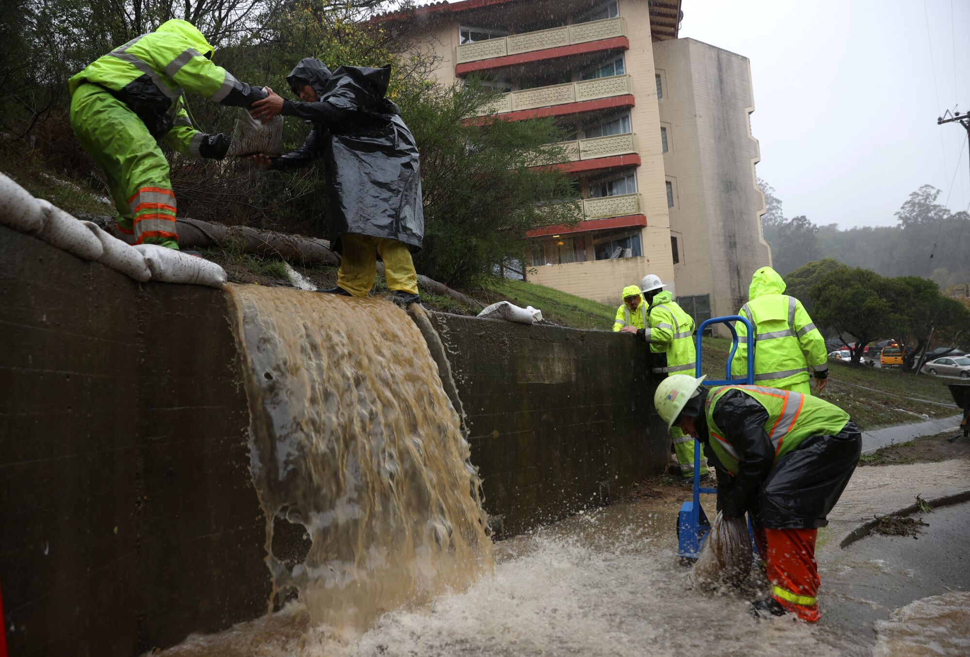 Workers try to divert water into drains as rain pours down Sunday in Marin City, Calif.