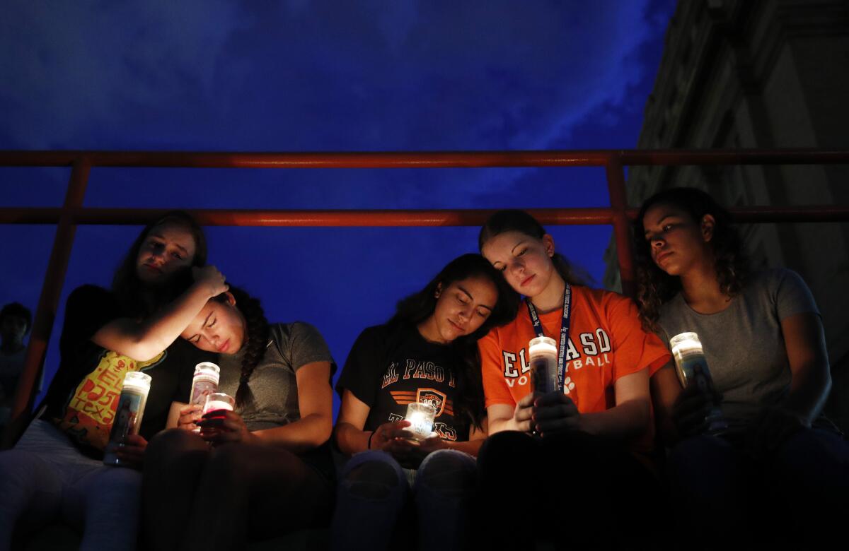 Mourners of the U.S. mass shooting in El Paso embrace each other at a vigil, seated with glowing candles.