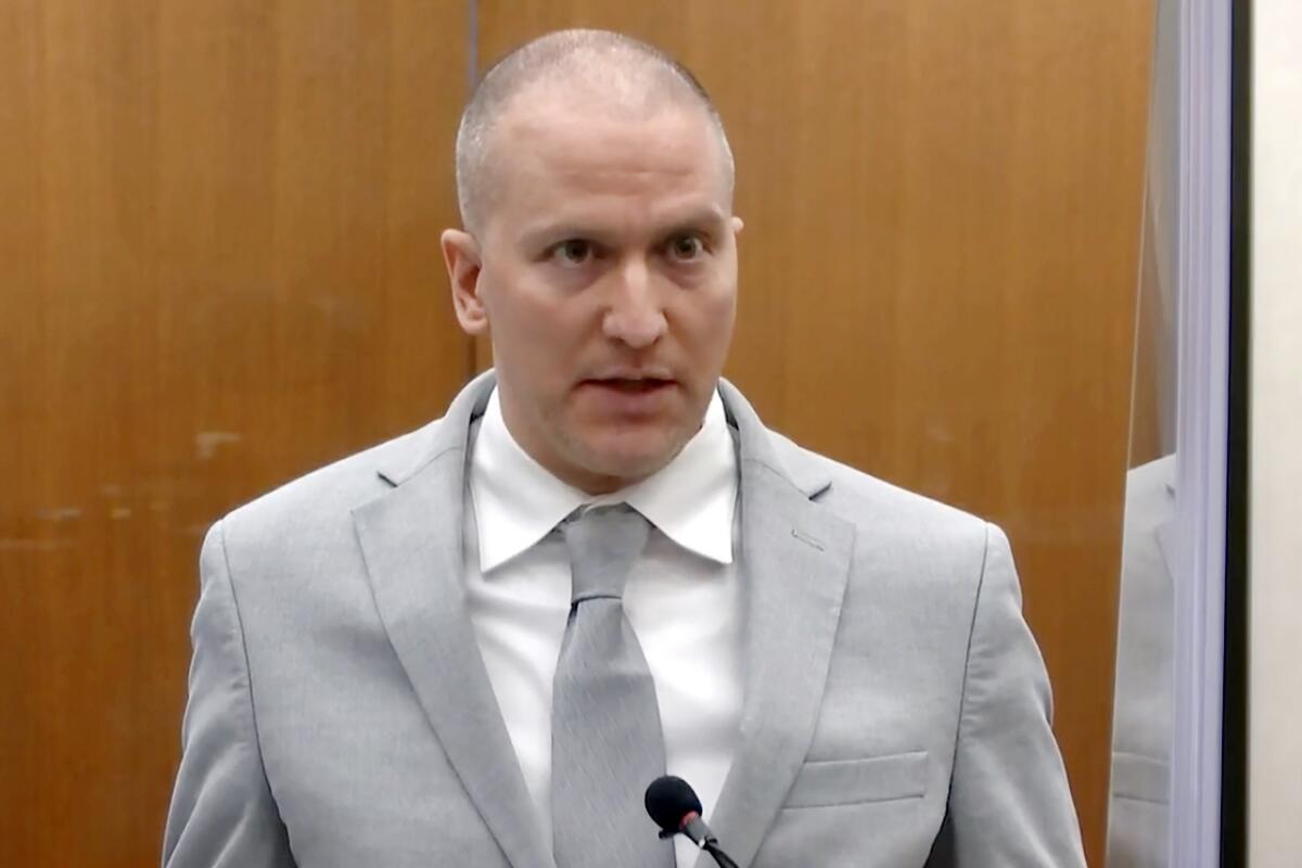 Derek Chauvin, wearing a gray suit and white shirt, speaks into a microphone in a courtroom 