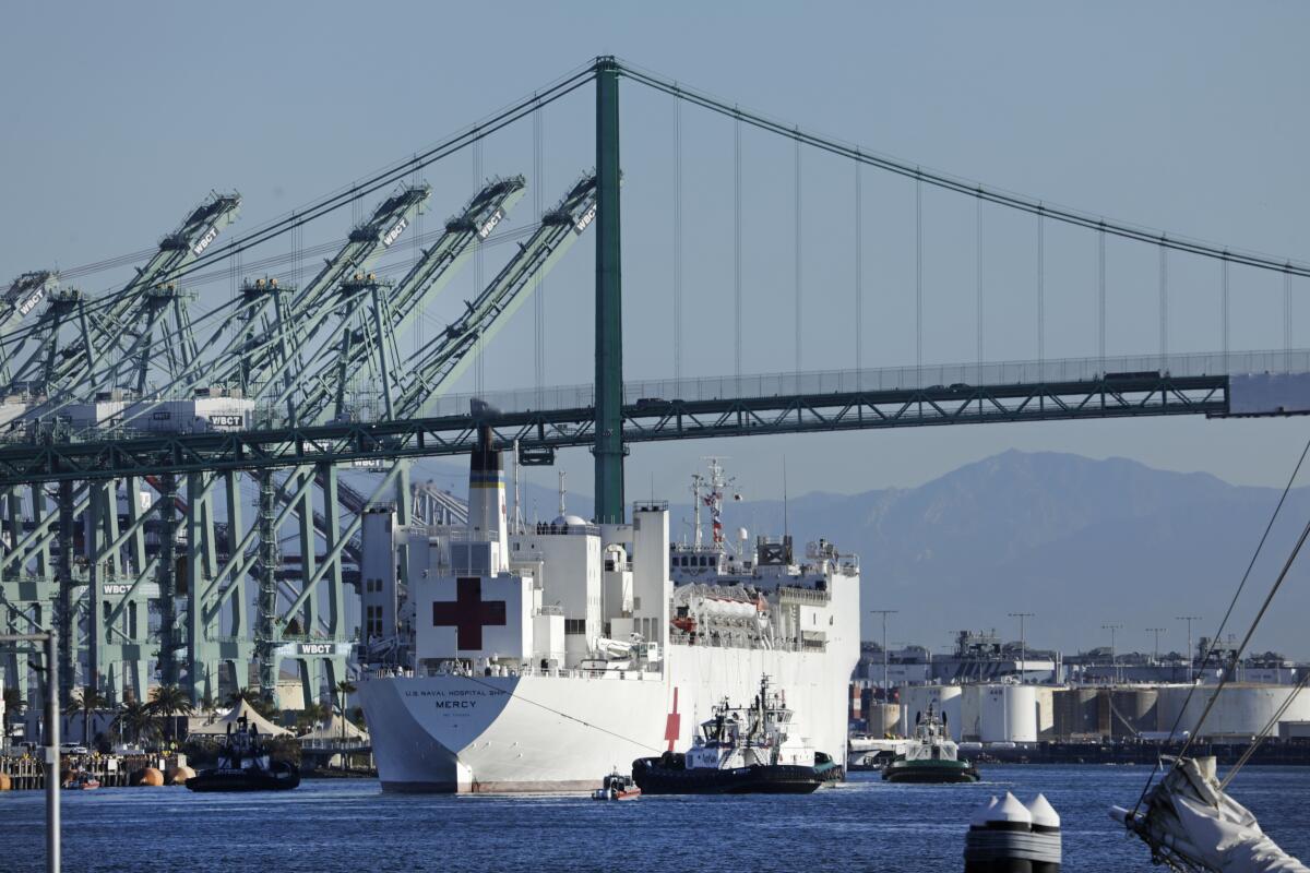 A large, white hospital ship with red crosses painted on its sides sails through a port complex