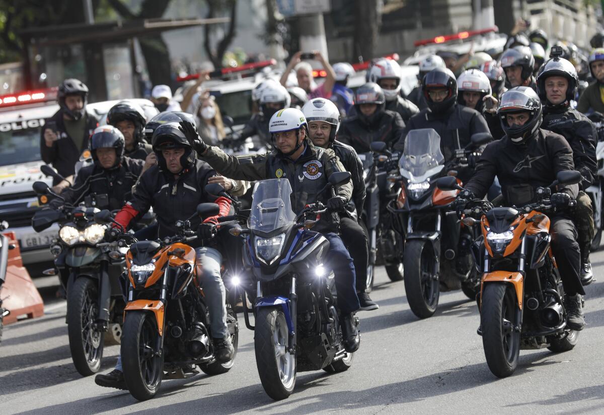 Brazil's President Jair Bolsonaro waves as he leads a caravan of motorcycle enthusiasts following him through the streets