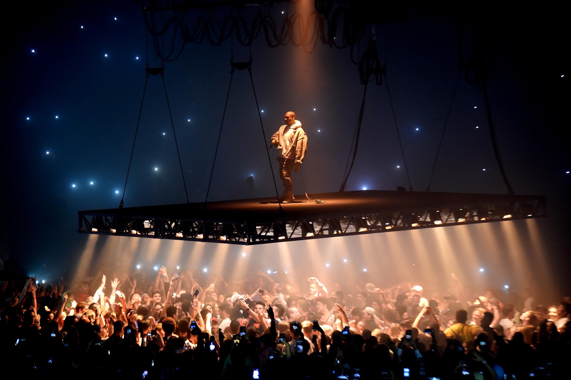 Kanye West performs on top of a platform suspended above a crowd