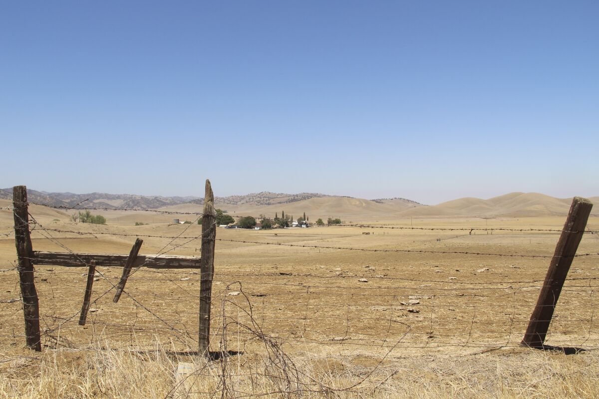 A dilapidated barbed-wire fence on dry, brown ranchland