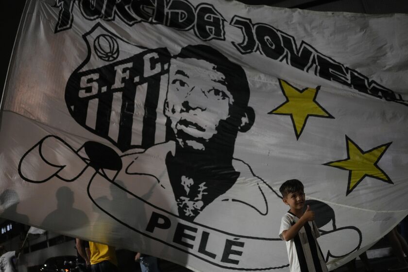 Un niño posa frente a una bandera de Santos, que muestra la efigie de Pelé, frente al estadio Vila Belmiro en esa ciudad brasileña, el jueves 29 de diciembre de 2022 (AP Foto/Matias Delacroix)