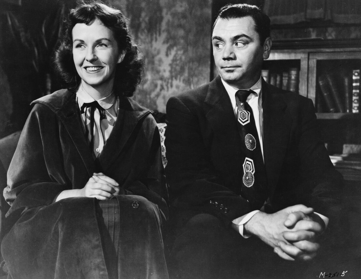 A black-and-white still of a woman and man sitting next to each other on a couch