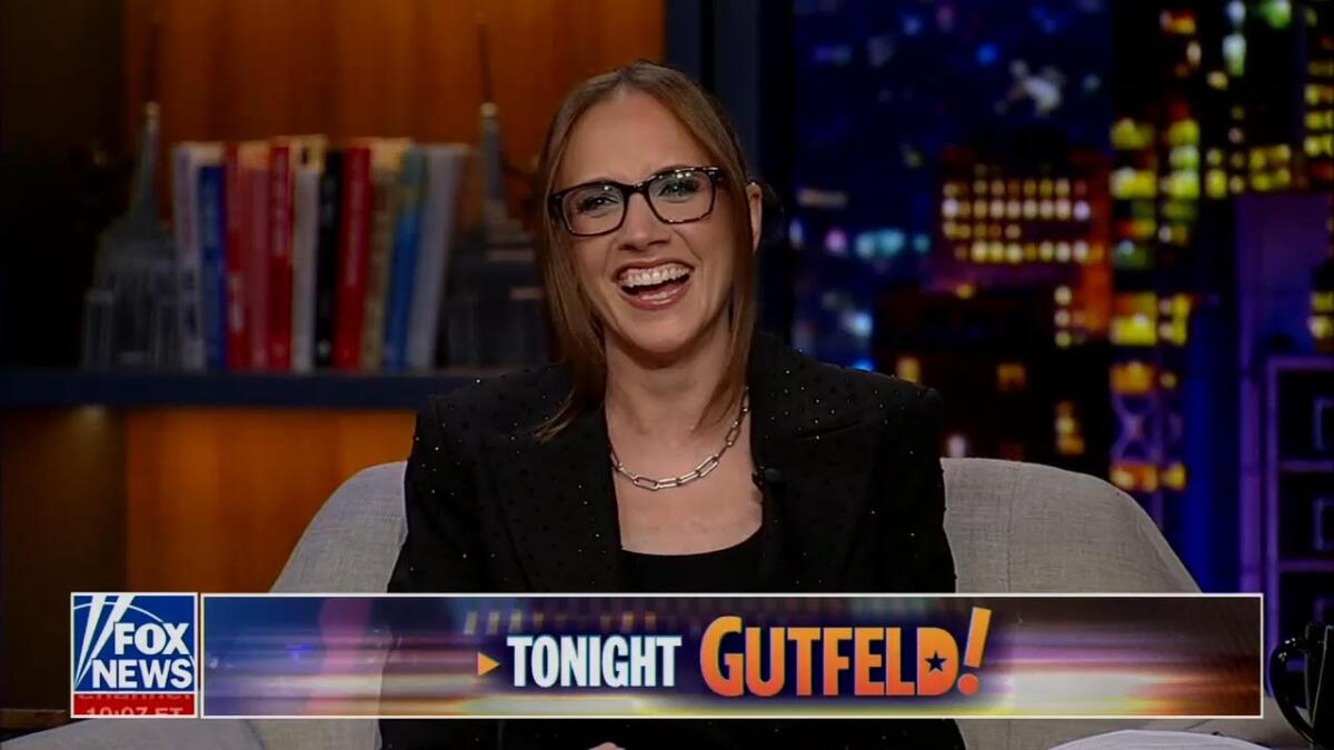 Kat Timpf laughs and smiles while seated in a beige chair on Fox News' late-night show "Gutfeld!"