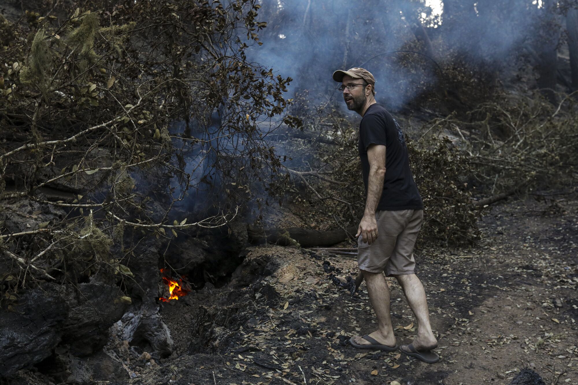 Noah Standridge, wearing flip-flops, walks on a blackened hill looking for hot spots near his home. 