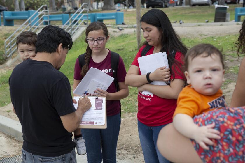 LOS ANGELES, CALIF. - JULY 23, 2019: America Barrera, 15, third from left, and Jimena Flores, 16, third from right, youth volunteers with CHIRLA, encourage Legnel Jimemez, who is holding son Andres Jimemez, 1, far left, to sign up for the census in MacArthur Park in Los Angeles, Calif. on Tuesday, July 23, 2019. Mother Janson Corado, who is holding son Anderson Jimenez, 6 months, far right, looks on. (Liz Moughon / Los Angeles Times)