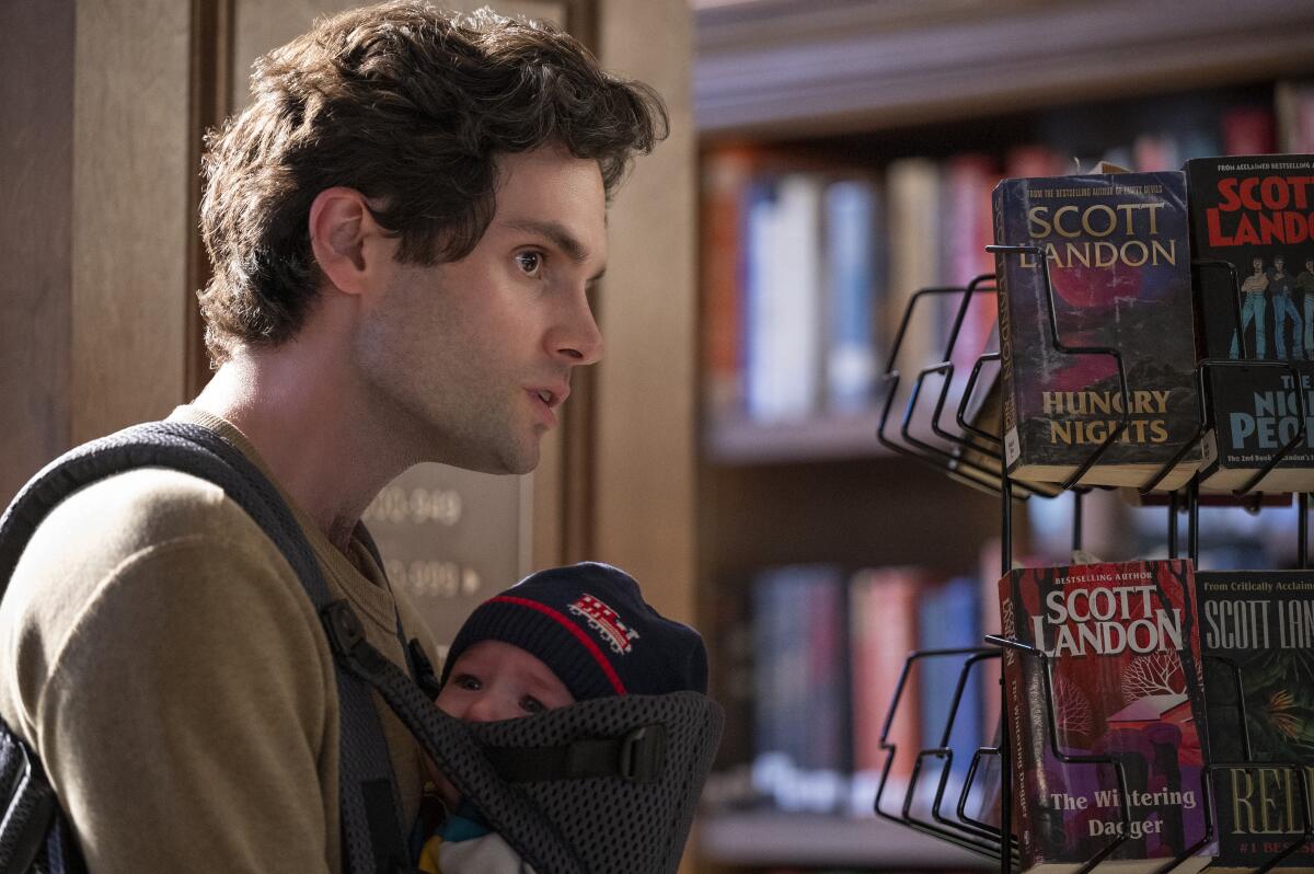 A man in a library with a baby in a carrier against his chest.