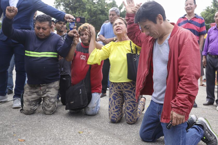 Residents pray as police officers come to the aid of a security guard who had a kind of vest with explosives taped to his torso, in Guayaquil, Ecuador, Thursday, March 30, 2023. Police officers deactivated and destroyed the vest that unknown persons had tied with adhesive tape to the chest of the jewelry store guard. (AP Photo/Cesar Munoz)