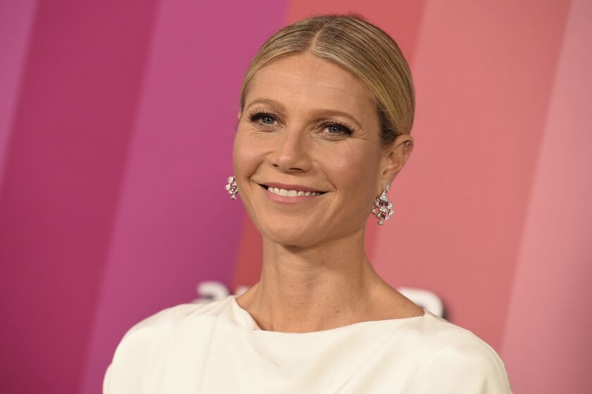 Woman, Gwyneth Paltrow, smiling at red carpet event in LA, wearing white with hair up in low bun, and jeweled earrings 