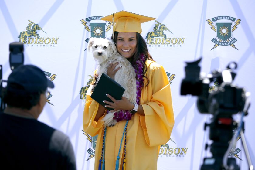 Kirstin Bui, 18 of Huntington Beach, holds her dog named Bailee while taking professional photos after receiving her diploma from Edison High School, during a drive-thru graduation ceremony at the school in Huntington Beach on Thursday, June 11, 2020.