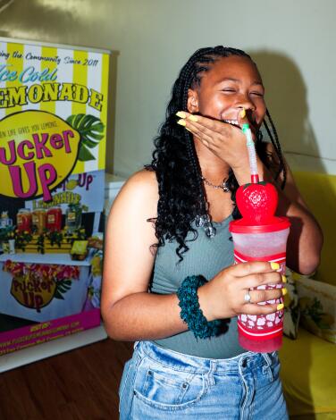 A laughing woman holds a large plastic cup with a plastic strawberry on top with a straw coming out of it