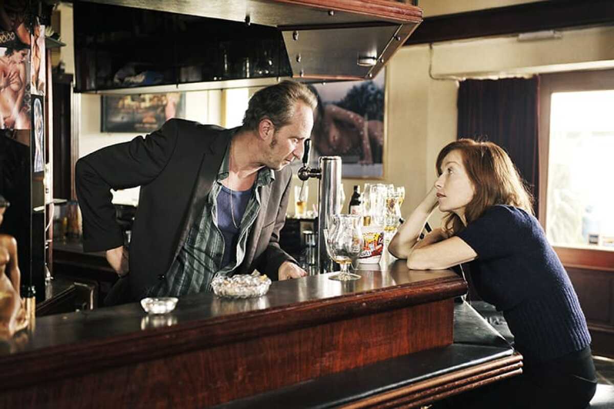 A man leans over a bar to talk to a seated woman.