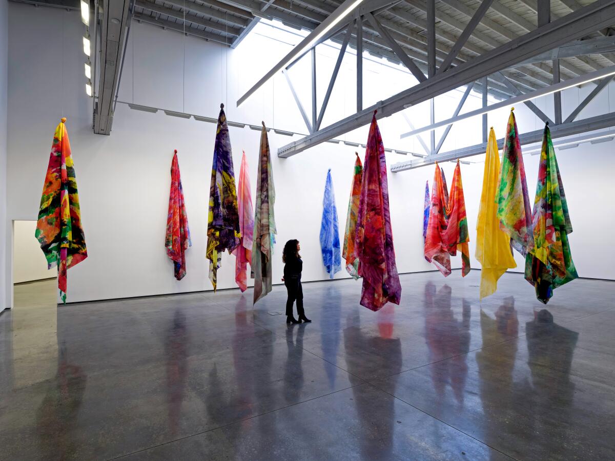Someone walking through a gallery with hanging colored drapes.