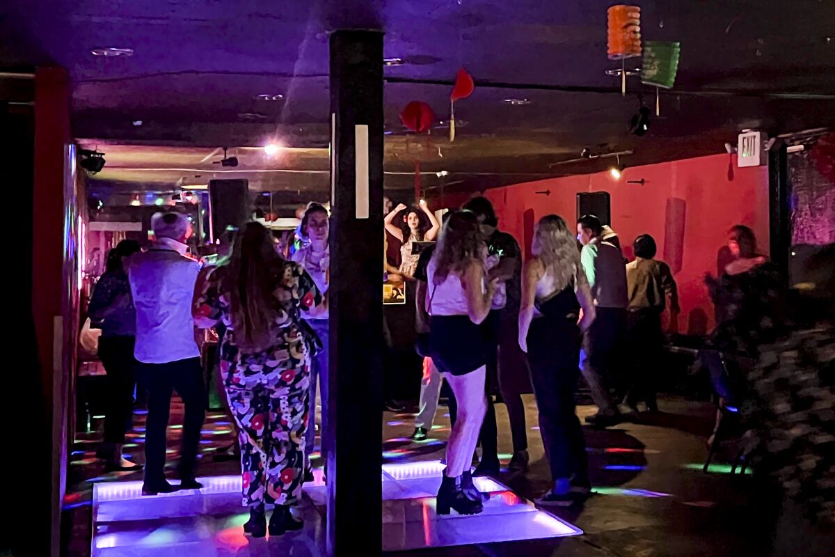 A '60s dance party with people dancing on a small dance floor under colorful lights