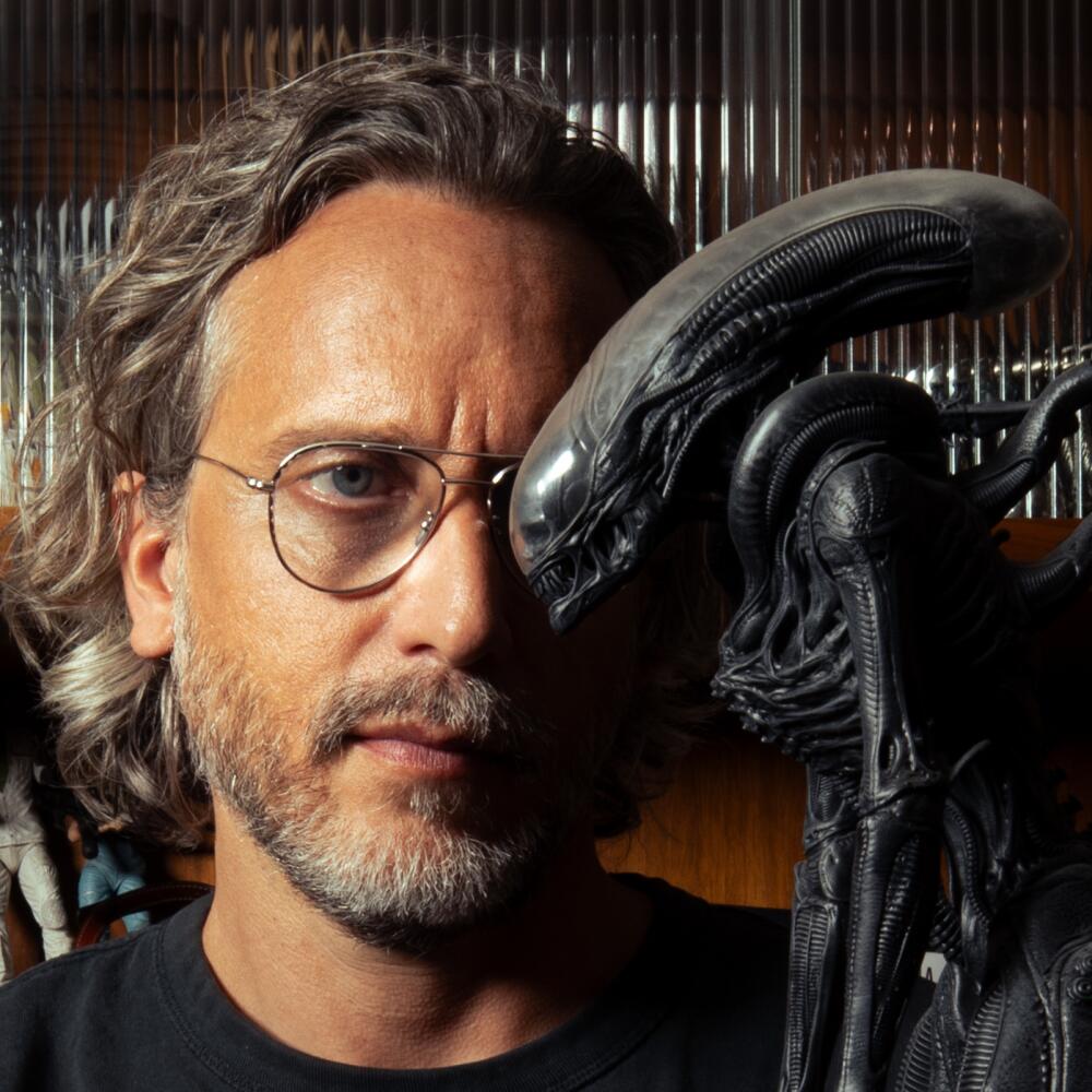 A bearded film director poses with a figurine of a scary, toothsome alien.