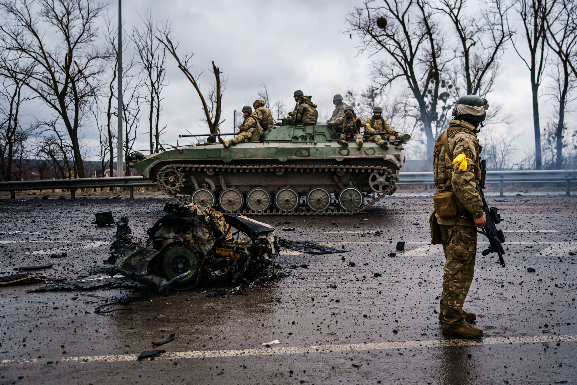 Uniformed troops ride a military vehicle on a debris-littered road