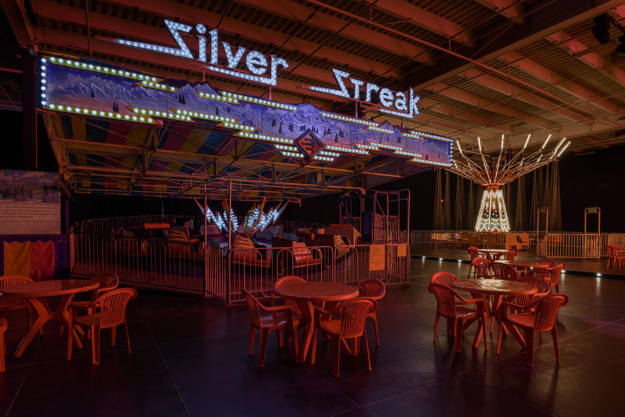 Inside a warehouse with tables and chairs set up with an amusement ride.