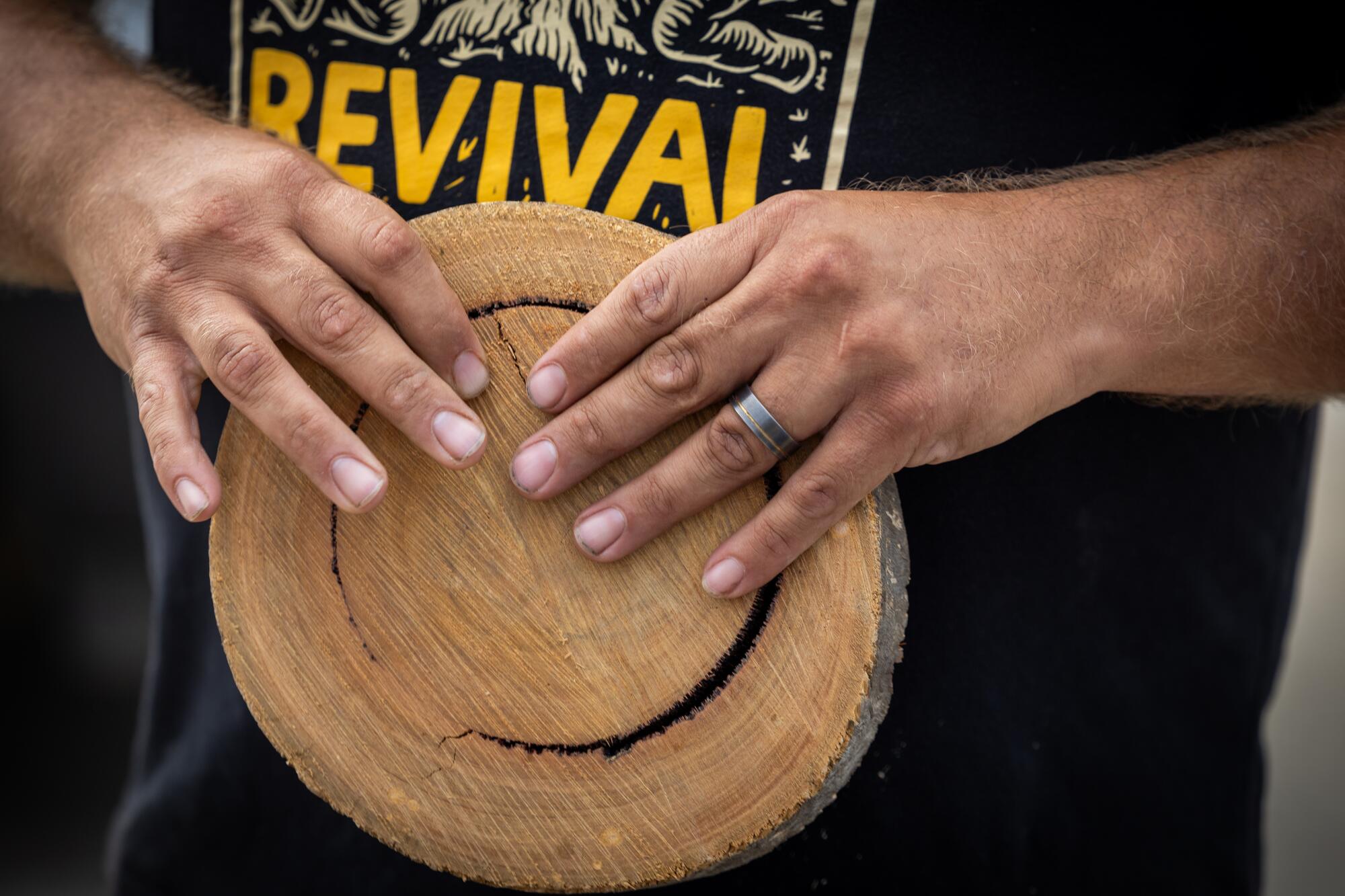 A man holds a thin, cross section of a tree trunk in his hands.