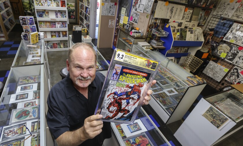 A man in a comic book store holds up a copy of "The Amazing Spiderman" in a plastic sleeve 