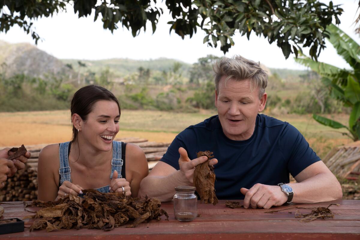 A man and a woman practicing rolling cigars at a picnic table.