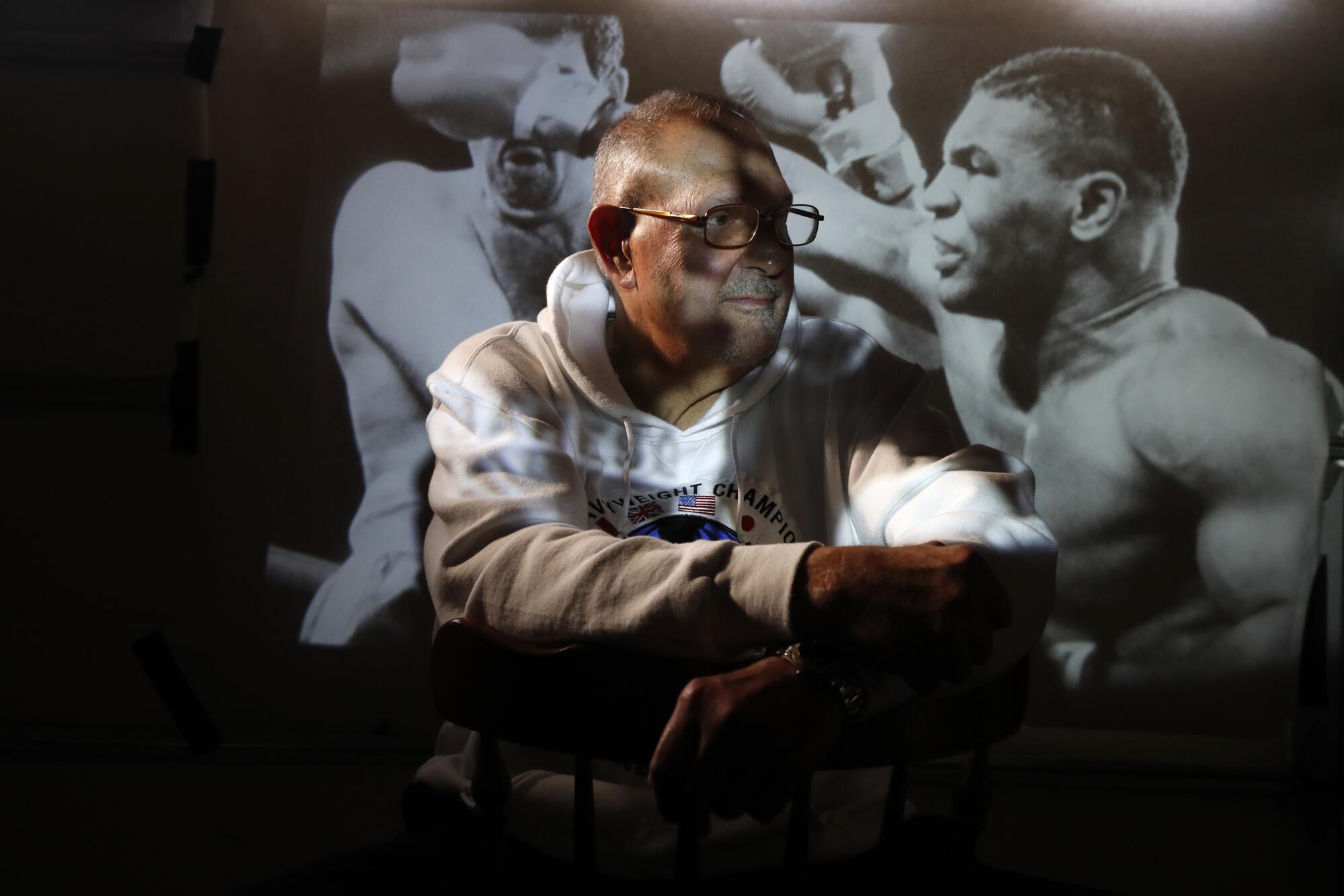 "Irish" Mike Jameson is shown in the shadows in front of a photo of two men boxing.