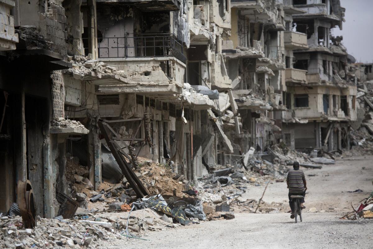 In this file photo taken on June 5, 2014, a man rides a bicycle through a devastated part of Homs, Syria.