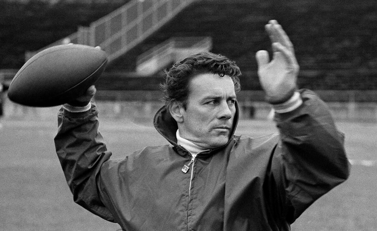 A man in a windbreaker cocks his arm to throw a football