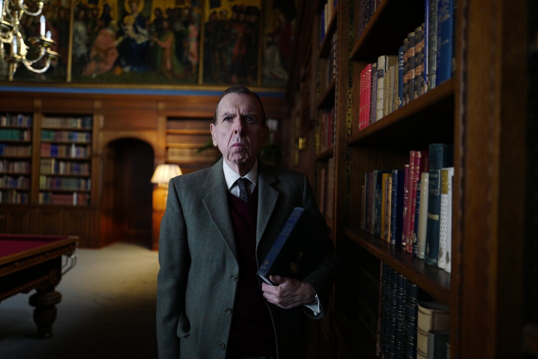 A man in a suit stands in a wood-paneled library.