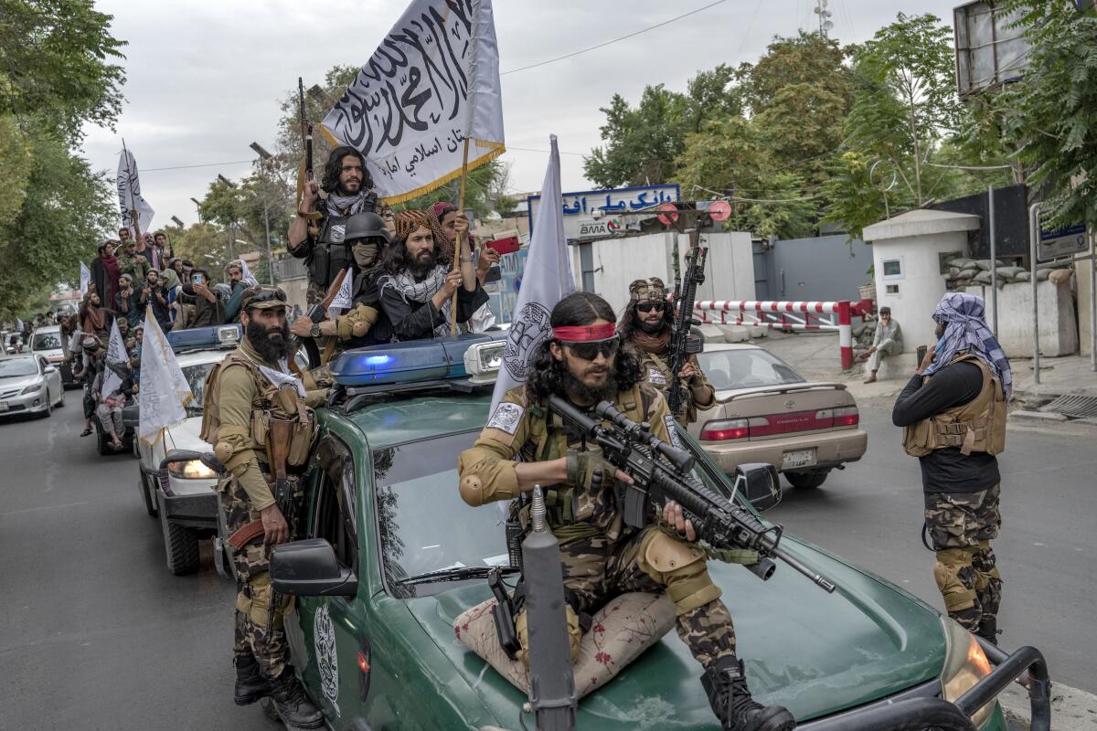 Men holding guns and banners ride in vehicles.