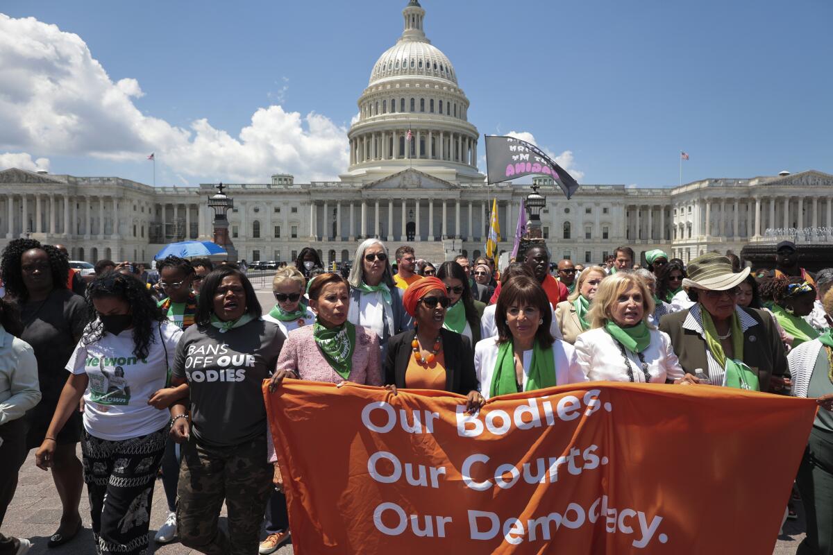 People march and hold a banner that says "Our bodies. Our Courts. Our Democracy," with a domed building in the background.