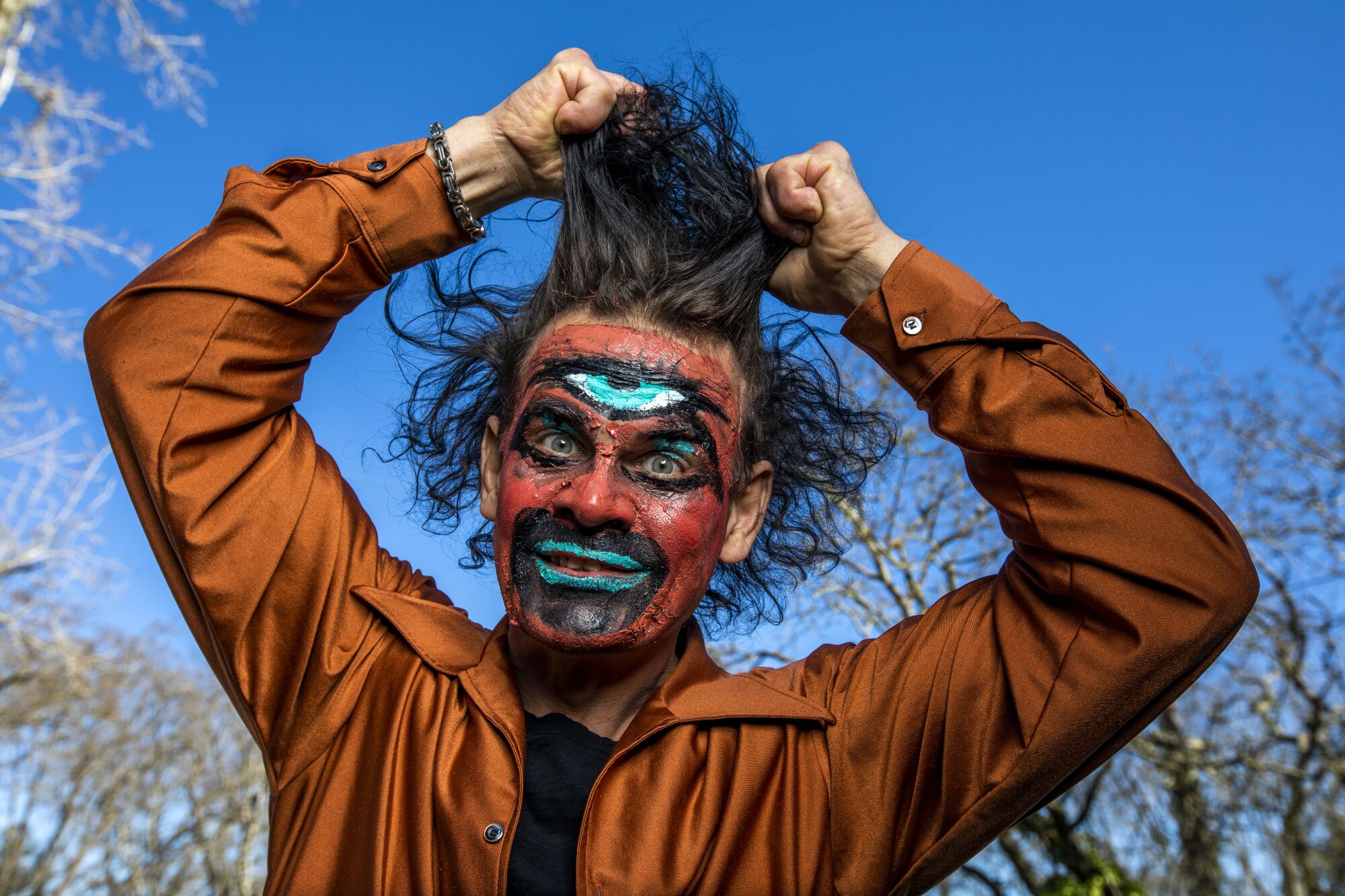 A man wearing blue, black and red face paint pulls at his hair with his hands.