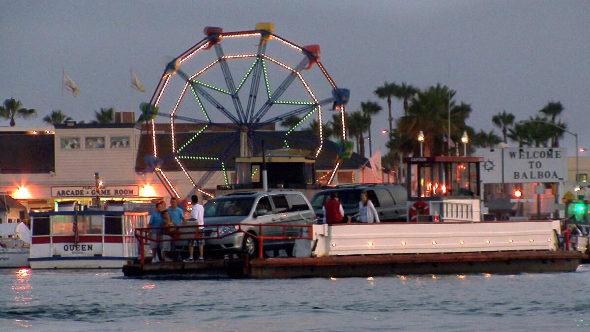The Ferris wheel at the Balboa Fun Zone is lit up behind one of the ferries shuttling cars and pedestrians.