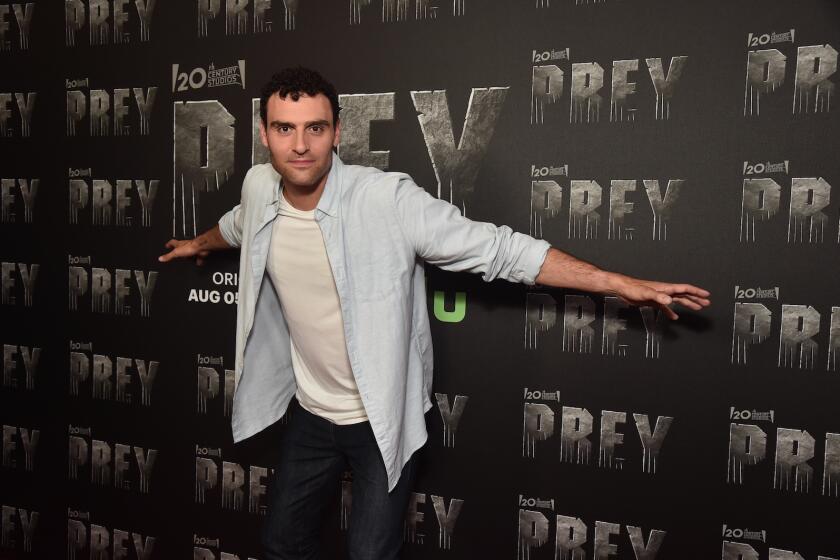 A man spreads his arms while standing in front of promotional material for the movie "Prey."