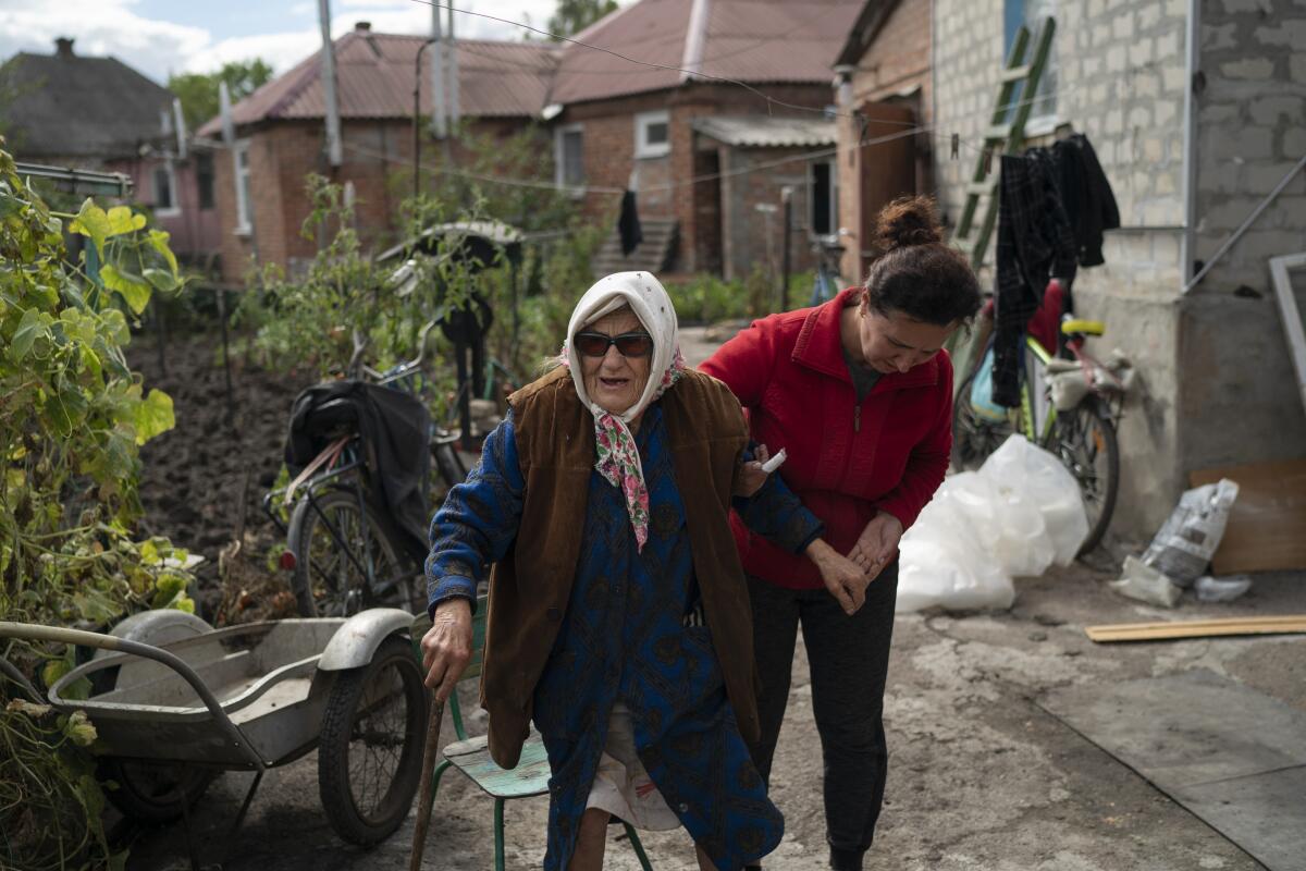 Mariia Ruban, de 92 años, recibe ayuda de una vecina para caminar por el jardín de su casa, 