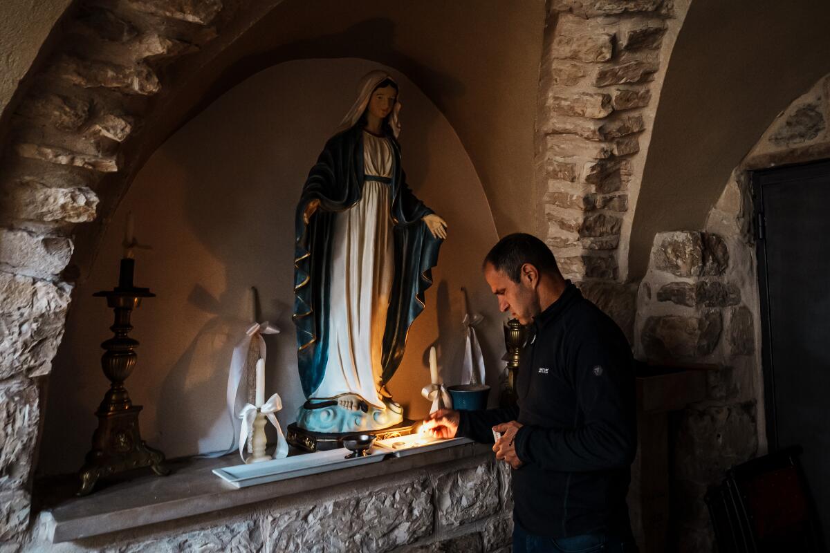A person lights a candle next to a statue of Mary.