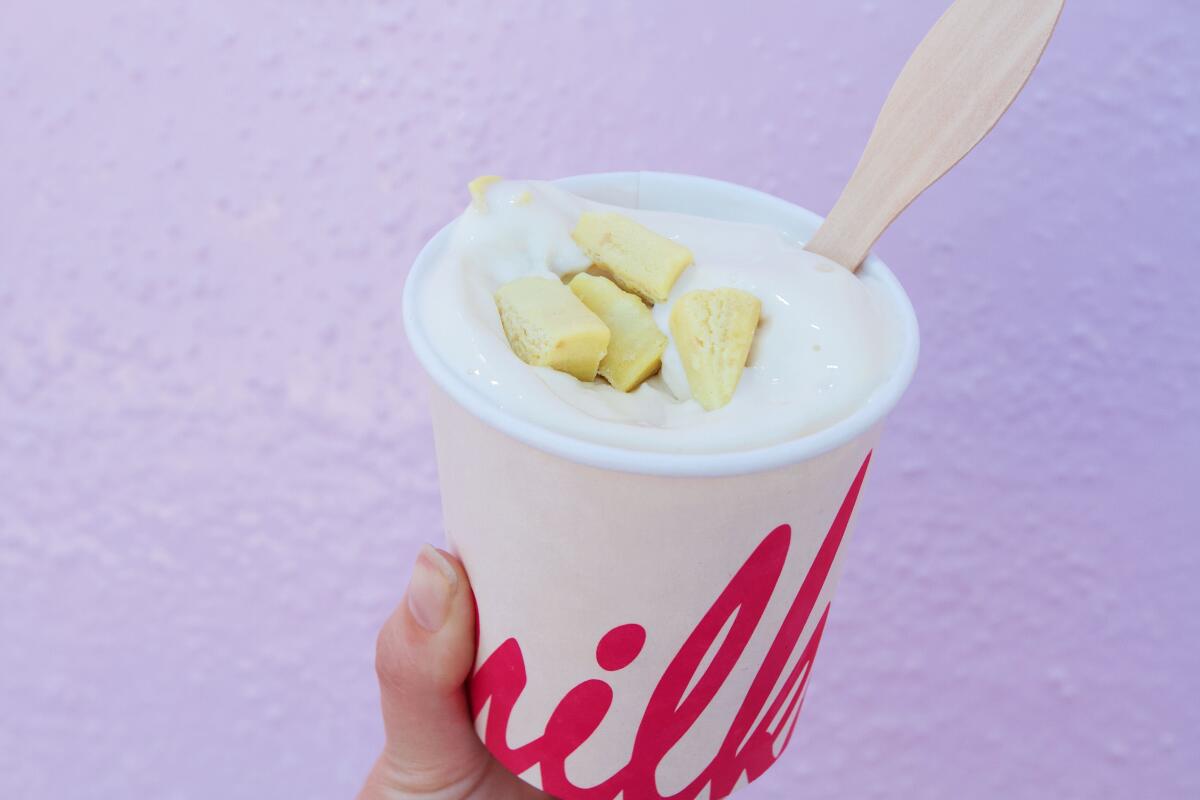 A hand holds a white cup of cereal milk soft serve quake from Christina Tosi's Milk Bar against a pink wall in L.A.