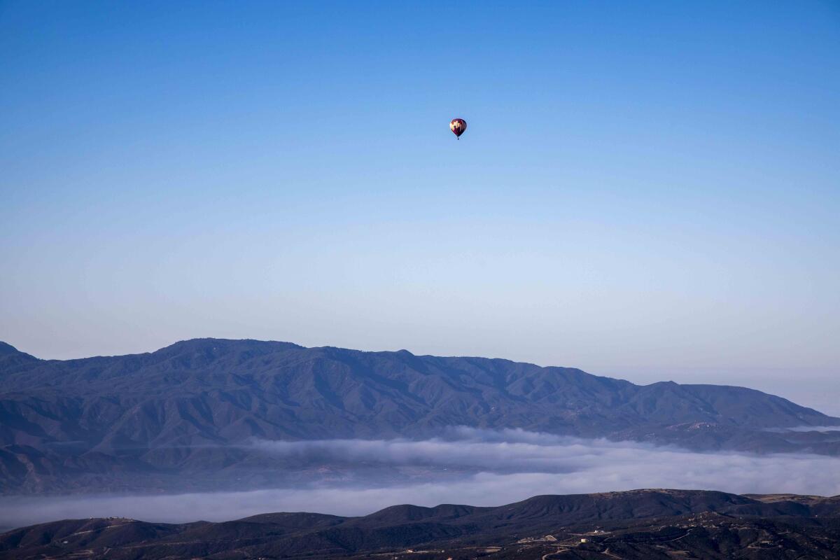 A hot air balloon is seen in the distance over rugged mountains and low fog.