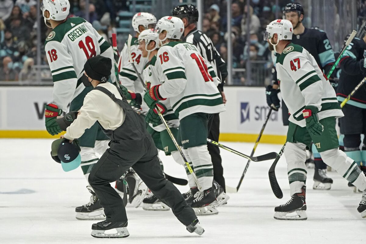 A worker picks up hats that were thrown onto the ice after a hat trick by Minnesota Wild center Rem Pitlick (16) against the Seattle Kraken during the second period of an NHL hockey game Saturday, Nov. 13, 2021, in Seattle. (AP Photo/Ted S. Warren)