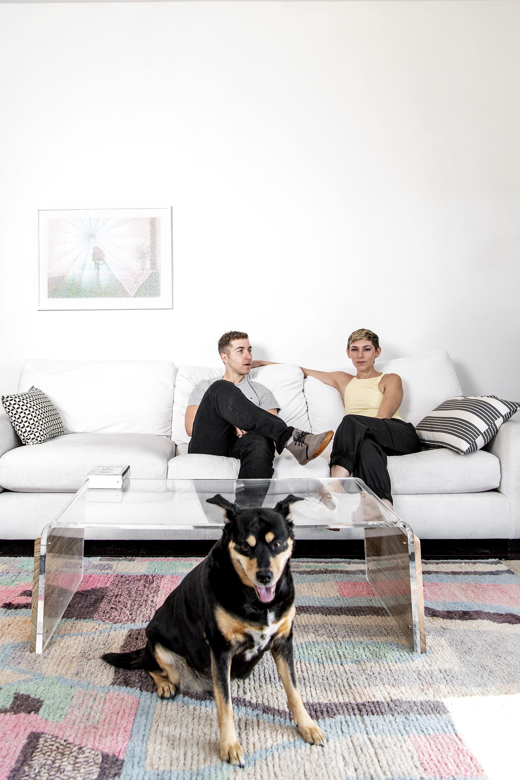 A couple poses on a white couch, with their dog in the forefront.