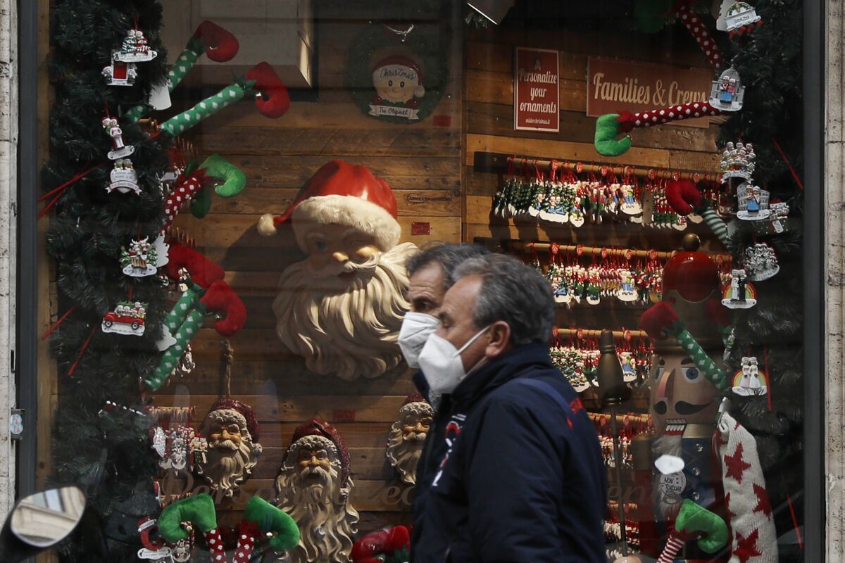 People walk past a shop window adorned with Christmas decorations, in Rome Tuesday, Dec. 1, 2020. Still, the large number of daily new COVID-19 cases is worrying, Italian health experts said, especially with the approach of year-end holidays, which could prompt people to ignore social distancing rules and gather in large numbers to celebrate. (AP Photo/Gregorio Borgia)