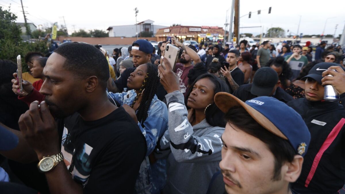 A crowd of people gathers at the scene where rapper Nipsey Hussle was killed in a shooting outside his clothing store in Hyde Park.