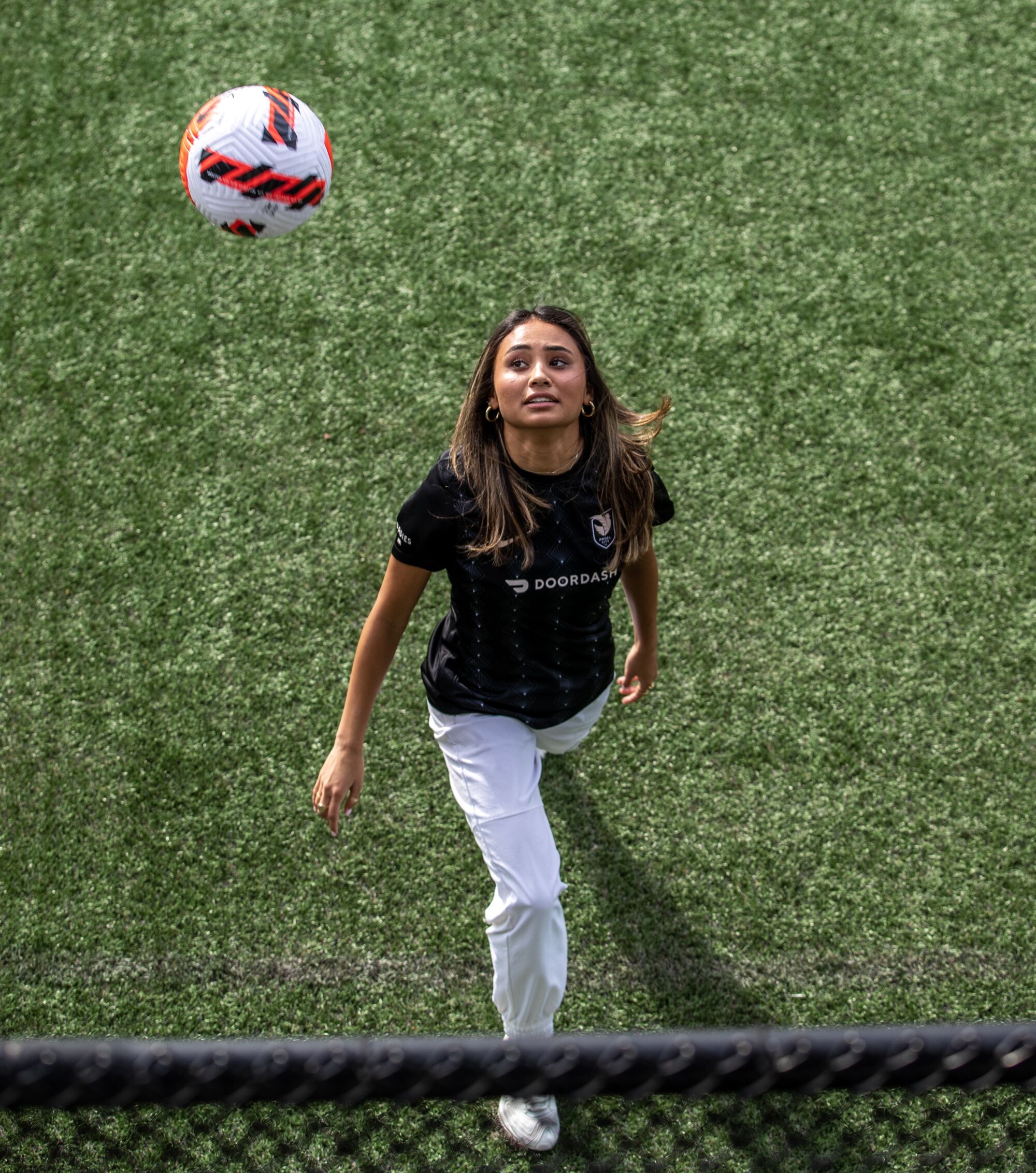Alyssa Thompson looks up at a soccer ball while standing on a field.