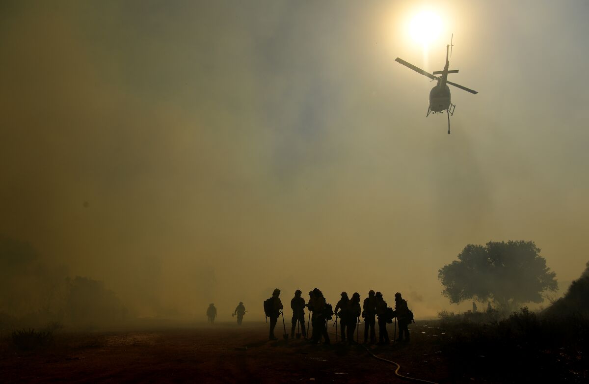 Several firefighters silhouetted in the smoke as a water-dropping helicopter flies overhead