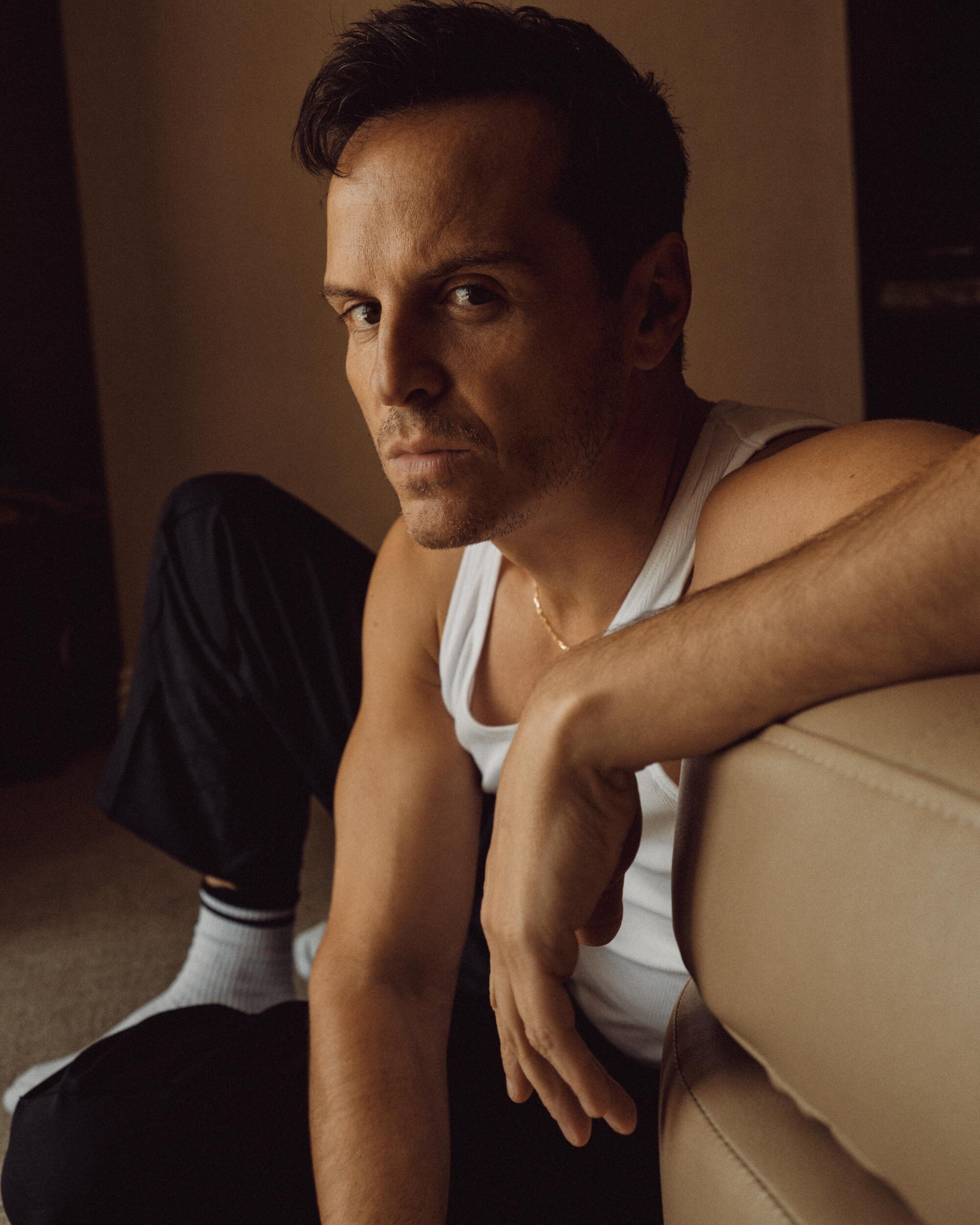 The actor sits on the floor and looks serious.